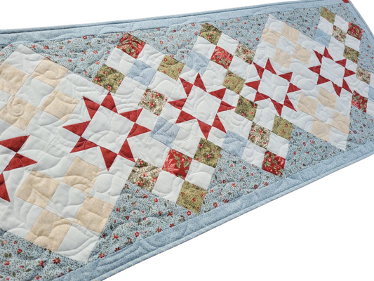 Quilted Christmas table runner in ice blue poinsettia fabric with green, ecru accents with red star patchwork blocks down the center.