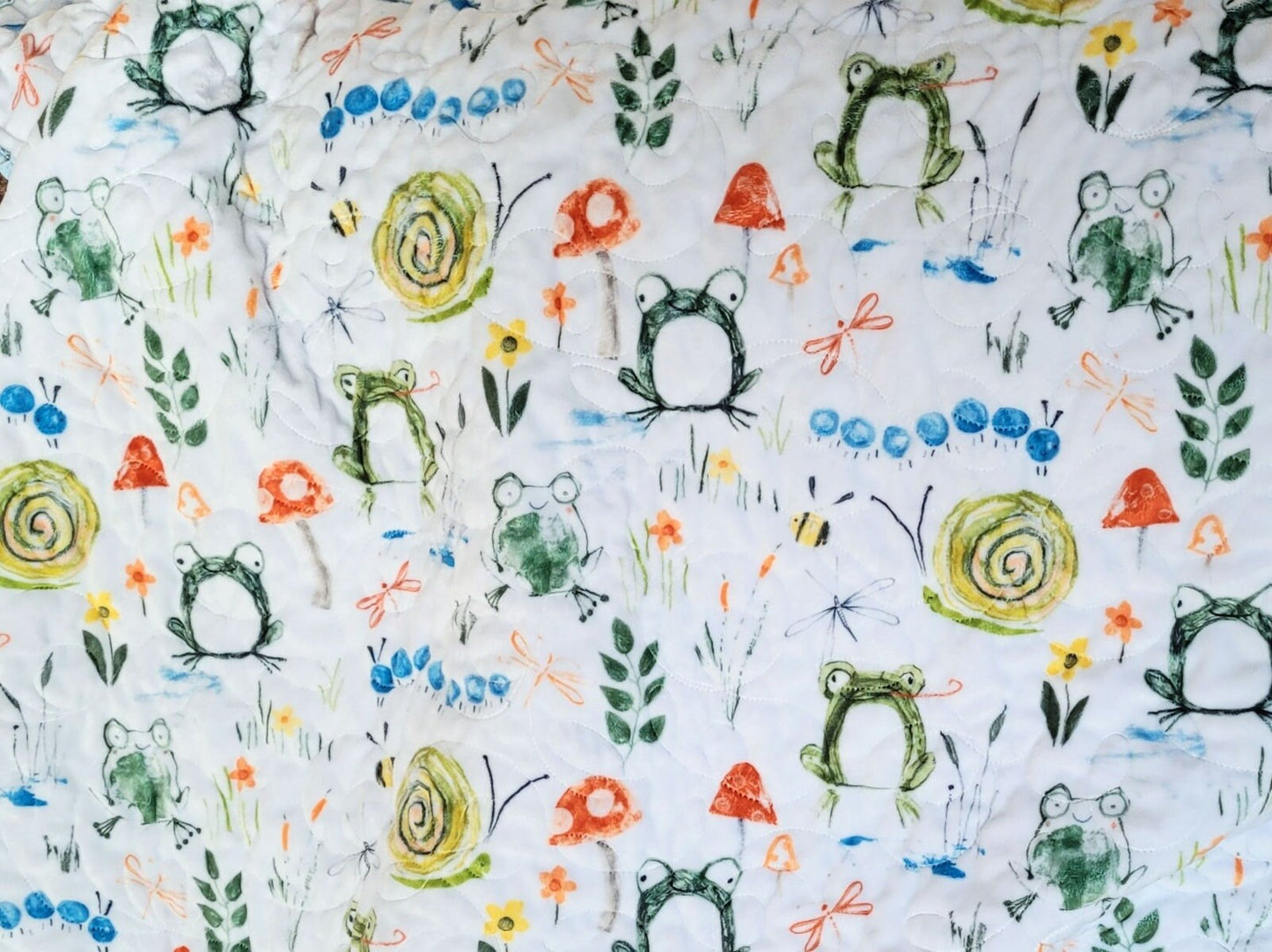 soft minky backing with frogs, snails, mushrooms, caterpillars, bees, flowers, grass and leaves.