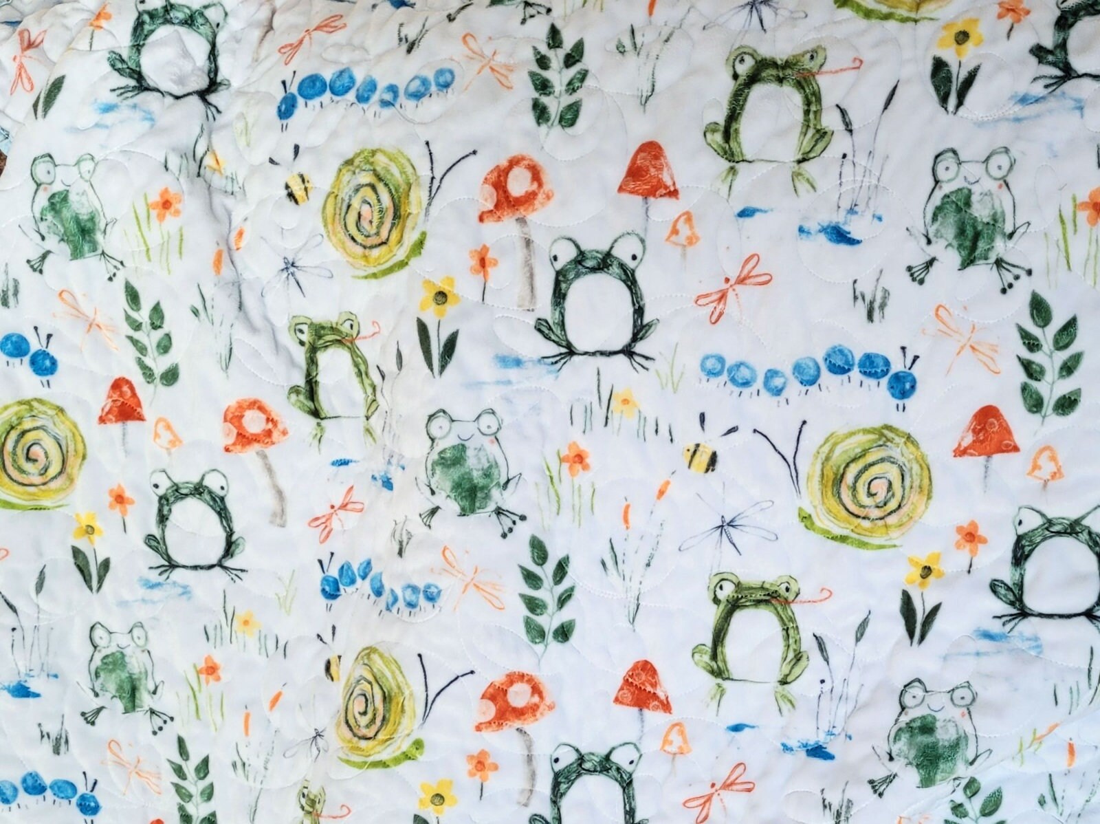 soft minky backing with frogs, snails, mushrooms, caterpillars, bees, flowers, grass and leaves.